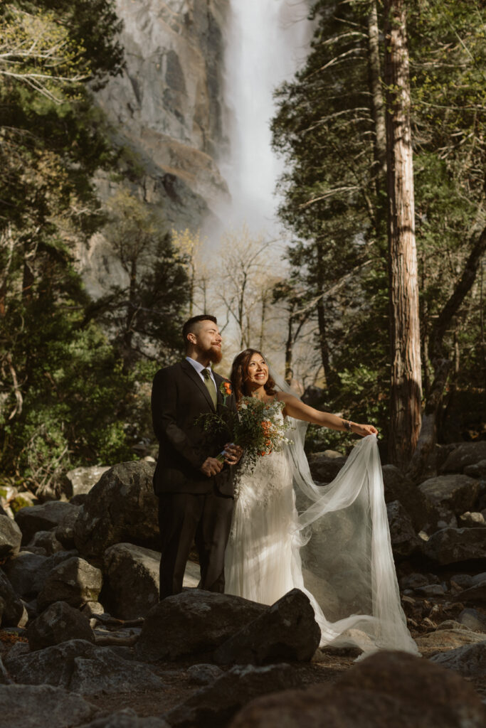 Couple takes photos in front of Bridal Vail falls ion their Yosemite Elopement Day 