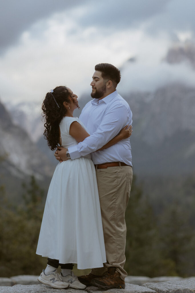 A couple embraces in the clouds on top of Tunnel view in Yosemite National Park, a Yosemite Park photographer capture the surprise proposal 