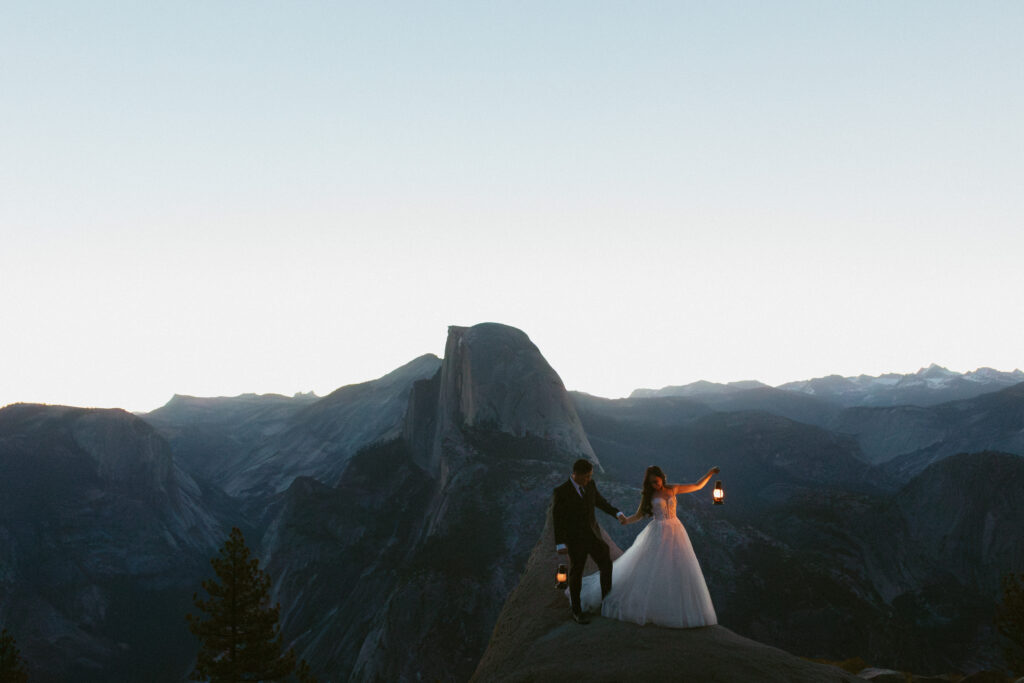 Sunrise wedding Portraits at Glacier point couple holds up lanterns inthe vast blue landscape 
