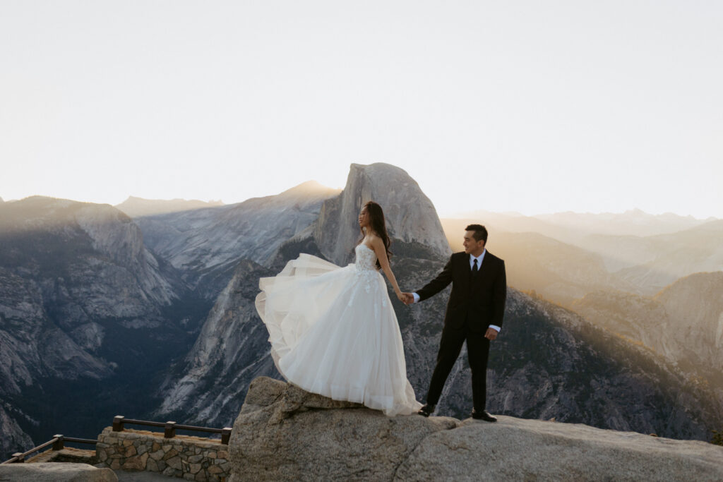 Sun rays light up the early morning behind half dome as couple dances for their portrait session 