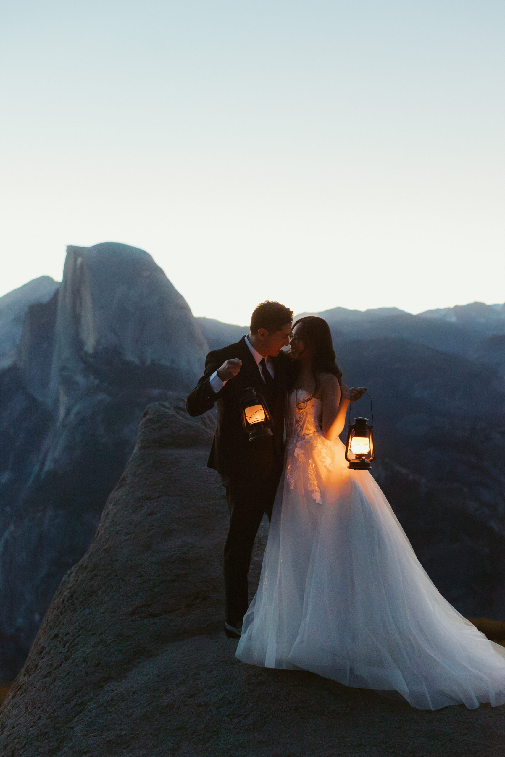 A couple share a kiss at glacier point while holding lanterns in the early morning light of their Yosemite wedding portrait session.