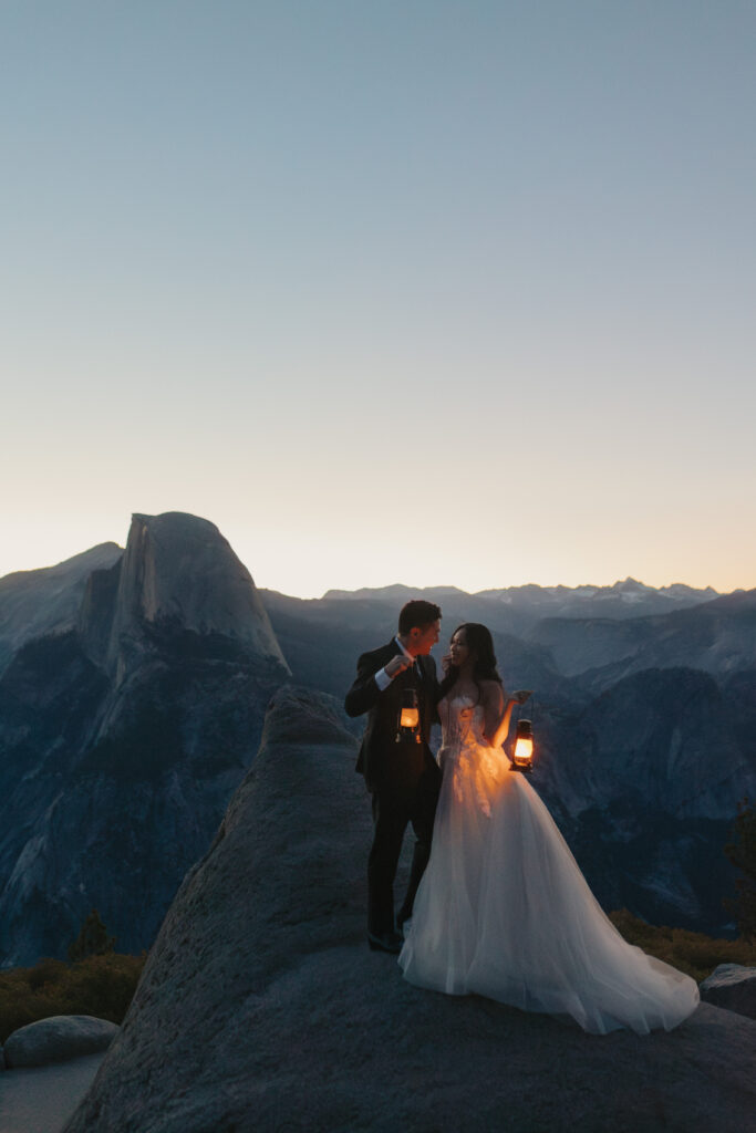 Couple holds up lanterns with the glacier point and half dome view behind them in the early morning hour light 