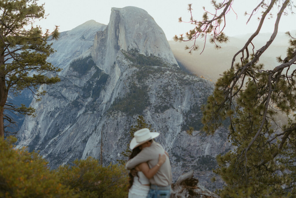 A couple Hugs in front of Half dome after their national Park Proposal 