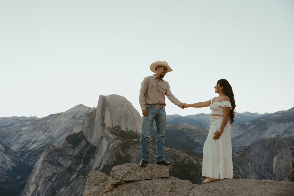 A couple stands in front of Half Dome Holding Hands 